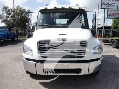 Truck image showing the front view of a white Freightliner Business Class M2Rollback truck with chrome grille, large bumper, and side mirrors.