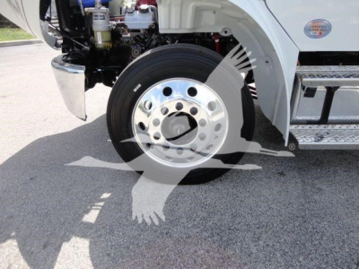 Truck front wheel assembly and partial cab area of a Freightliner Business Class M2 rollback truck showing chrome wheel, tire, and lower body components.