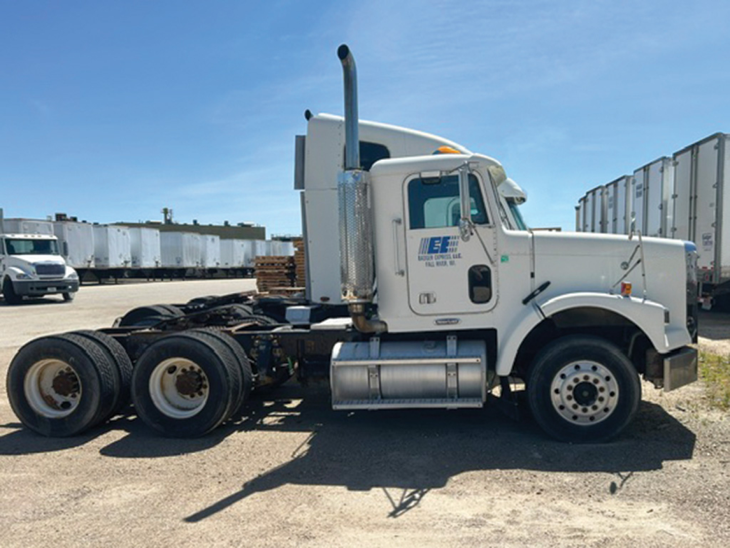 Truck chassis of a Freightliner FLD120 in-profile view showing cab, exhaust stack, fuel tanks, and dual rear axles. Side door text and logo visible on cab.