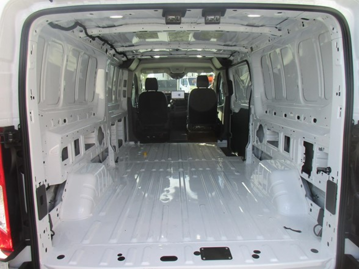 Cargo van interior of a 2026 Ford Transit with empty metal cargo area and front seats visible; cargo space shows bare metal floor and wheel wells.