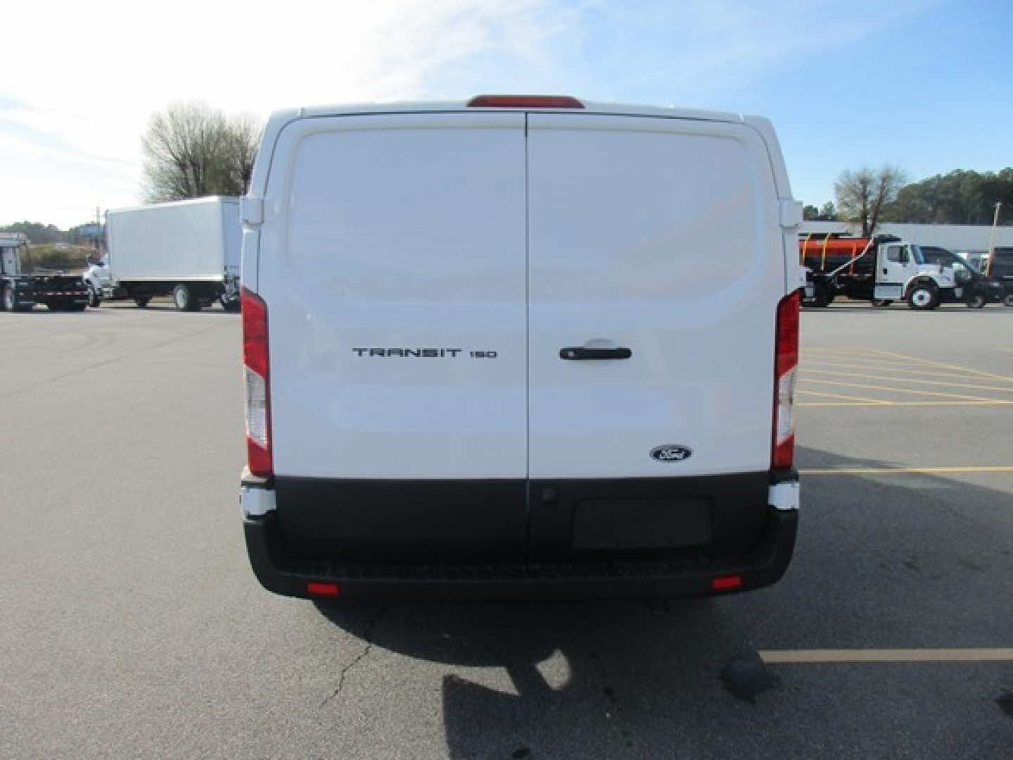 Ford Transit 250 cargo van rear view showing twin rear doors with Ford emblem and Transit badge; parking lot with other trucks in background.