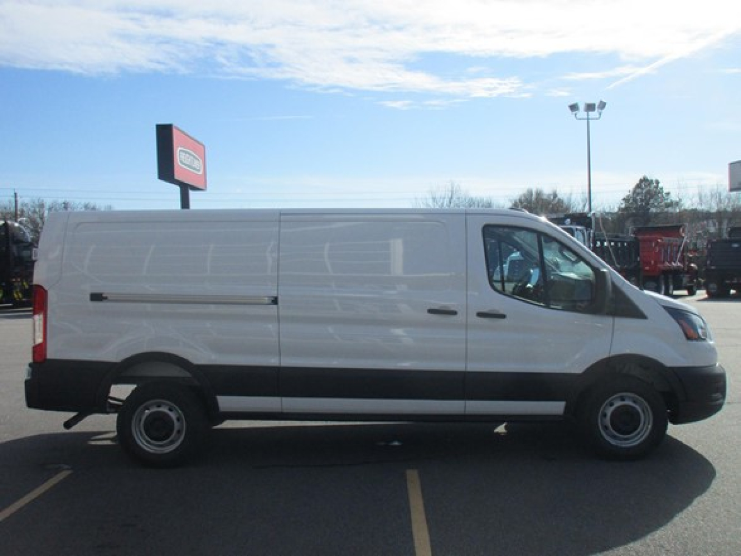 Ford Transit cargo van side profile showing blank white cargo area, black lower trim, steel wheels, daytime dealership lot.