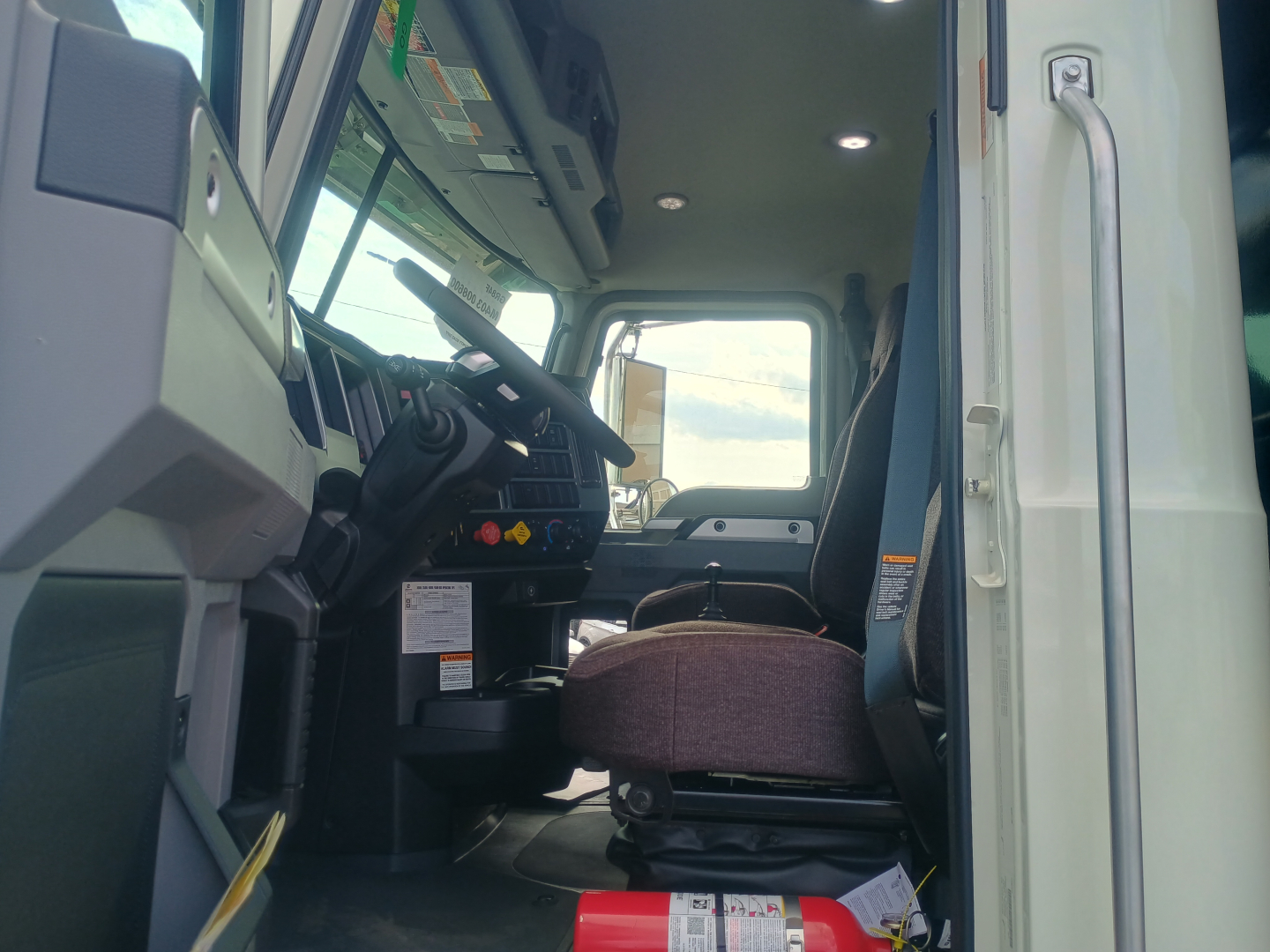 Truck cab interior of a new Mack GR84F dump truck showing driver's seat, steering wheel, dashboard controls, and part of the door frame.