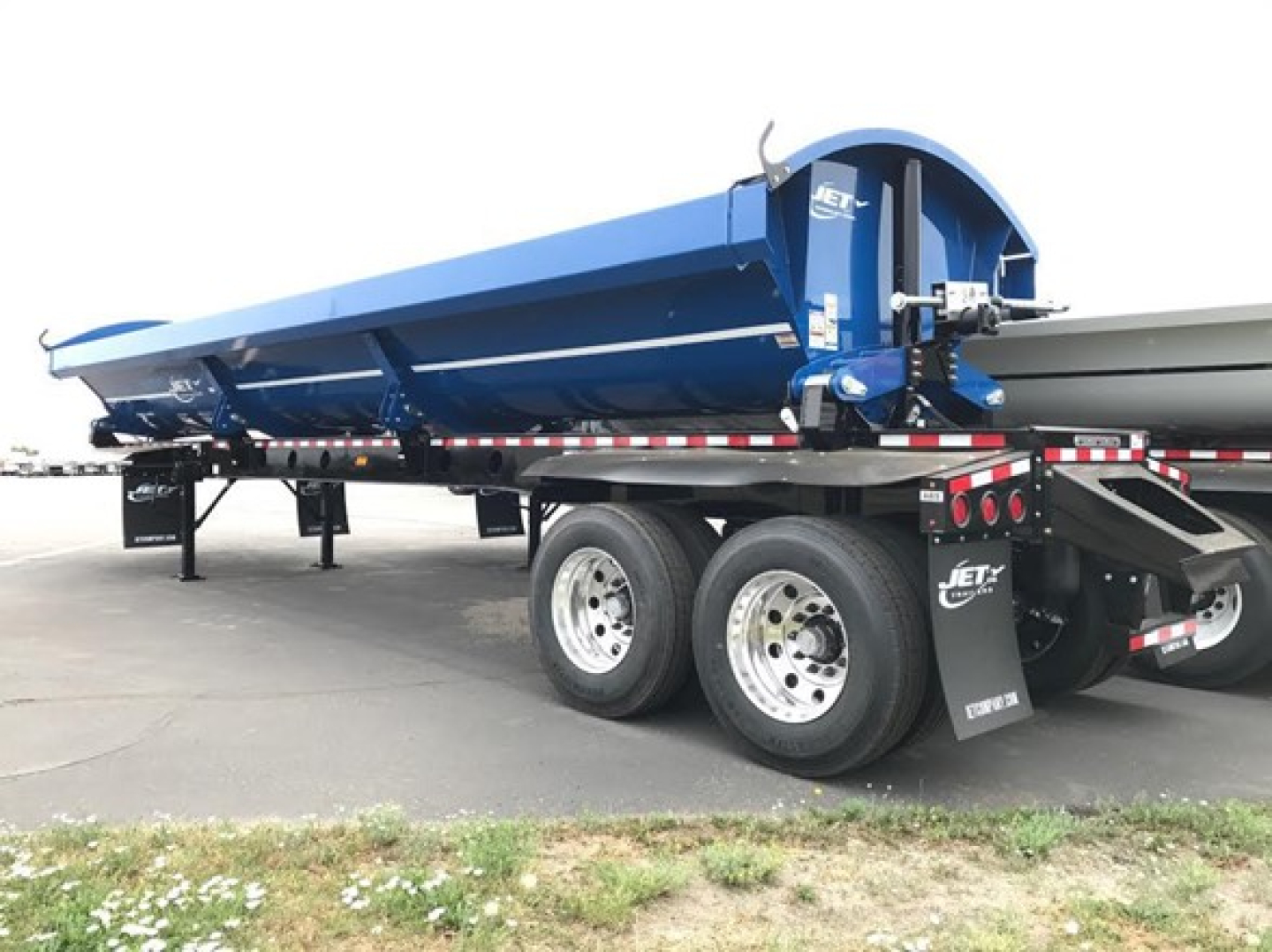Blue Jet Side Dump trailer in profile view showing hydraulic dump body and dual rear axles with black undercarriage and safety decals.