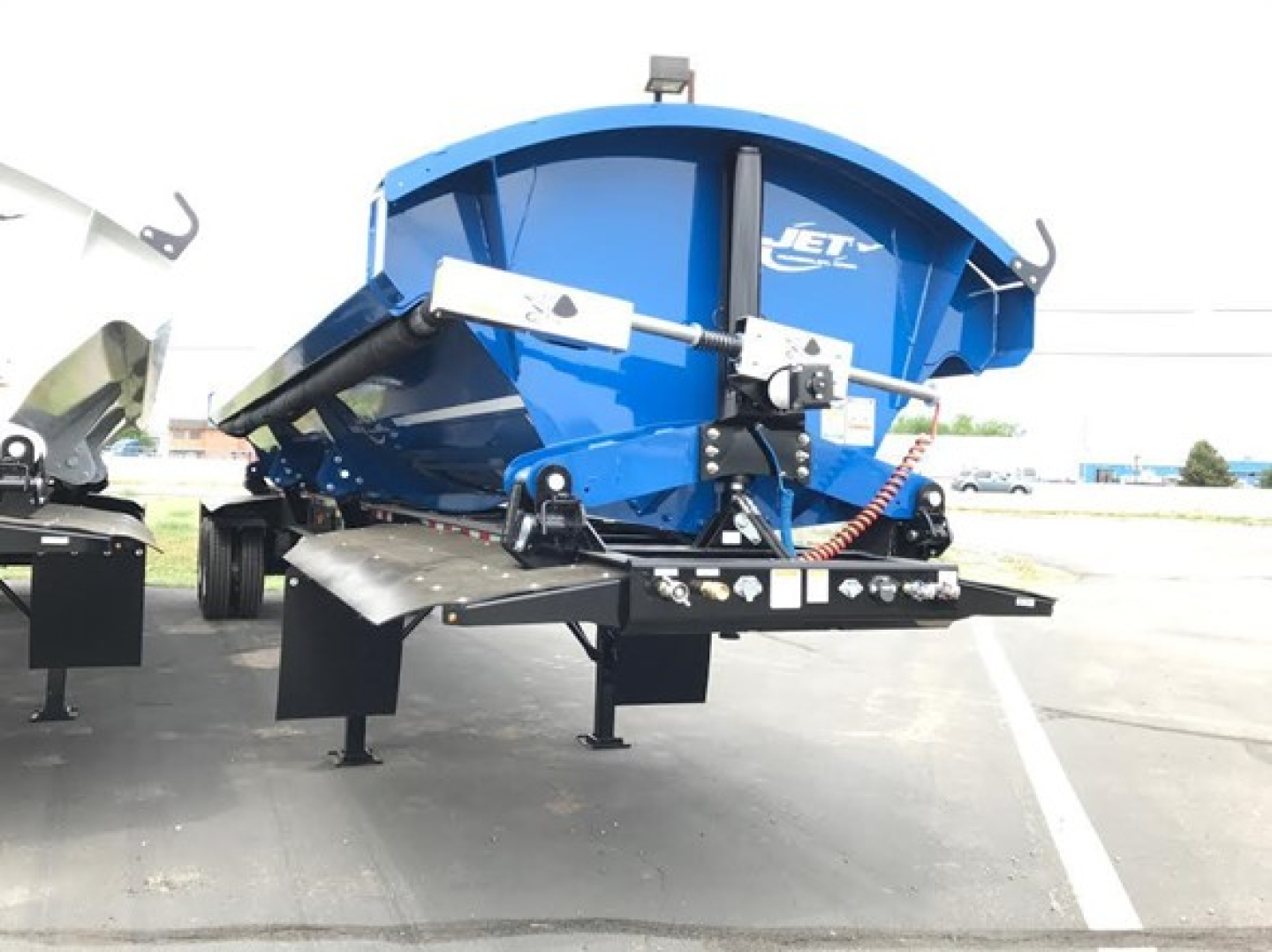Blue Jet side dump trailer on a trailer chassis, side view showing dumping mechanism and hydraulic lift arms.