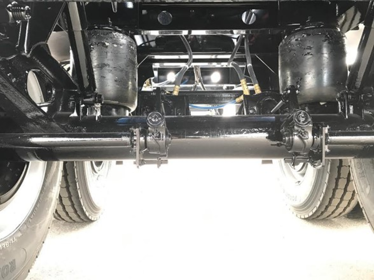 Understep view of a heavy-duty dump trailer chassis showing axles, suspension, and hydraulic lines.