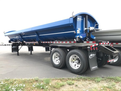 Jet Side Dump trailer showing blue bed and tandem axle wheels with rear mudflaps and reflective safety stripes.