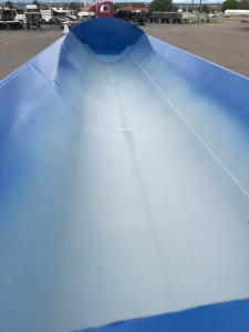Blue dump trailer interior with smooth metal walls and high sidewalls, view from the hopper looking toward the front.