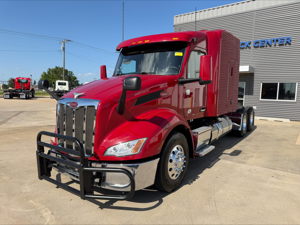 Peterbilt 579 truck in red, front three-quarter view, with large grille guard, chrome bumper, sleeper cab, side steps, and dual rear wheels.
