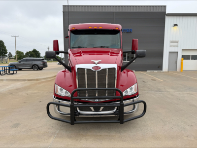 Peterbilt 579 front view with grille guard, red cab, large bumper, and side mirrors in a dealership lot.