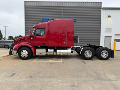 Peterbilt 579 tractor-trailer side view showing red cab, sleeper, chrome fuel tanks, and dual rear axles in a parking lot.