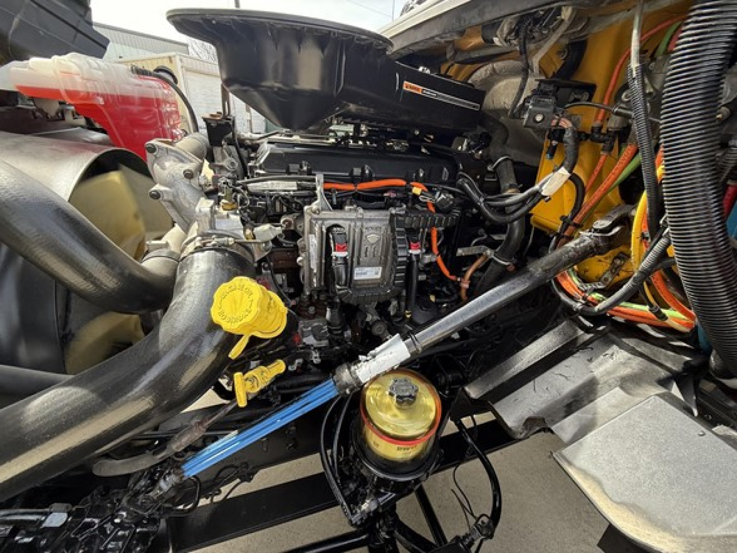 Engine bay of a 2019 International LT625 daycab showing yellow coolant reservoir cap, orange wiring, blue hose, and black engine components.