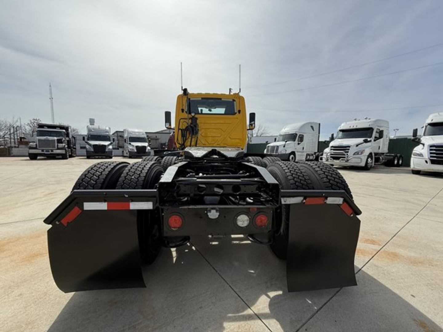 International LT625 truck tractor rear view showing mud flaps and fifth wheel setup, two rear axles with tires, and yellow cab in background.