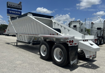 Dump trailer showing white CTS BDT-40 with dual rear axles and ramp, side rails, and branding; clear sky and trucks in background.
