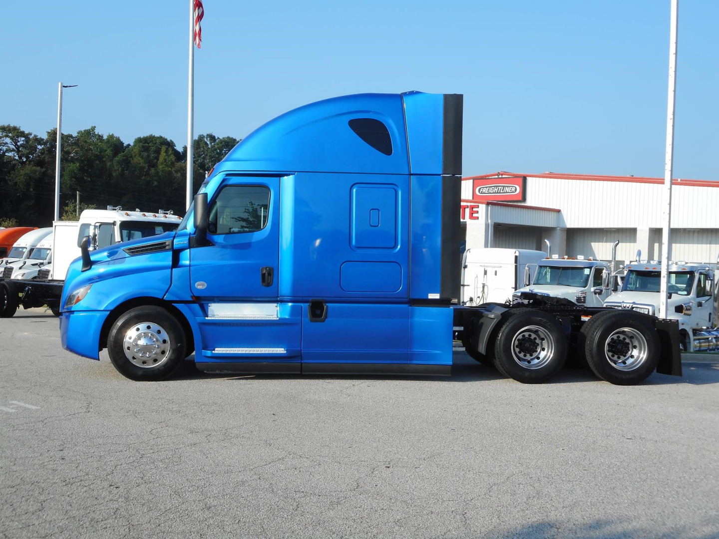 Truck tractor in blue showing cab profile and sleeper with 6x4 rear wheels at a dealership