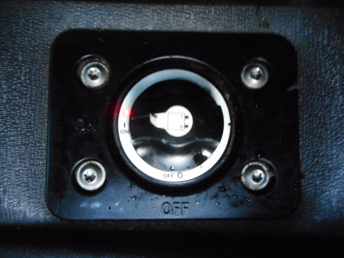 Circular switch with OFF/ON markings mounted on a textured surface, four screws at corners, small water droplets around, close-up view.
