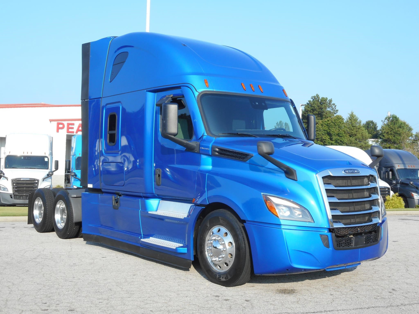 Truck cab showing a blue 2022 Freightliner Cascadia 126 conventional sleeper tractor parked, with chrome wheels and dual rear axles, VIN 3AKJHHDR6NSNA1705 displayed in listing.