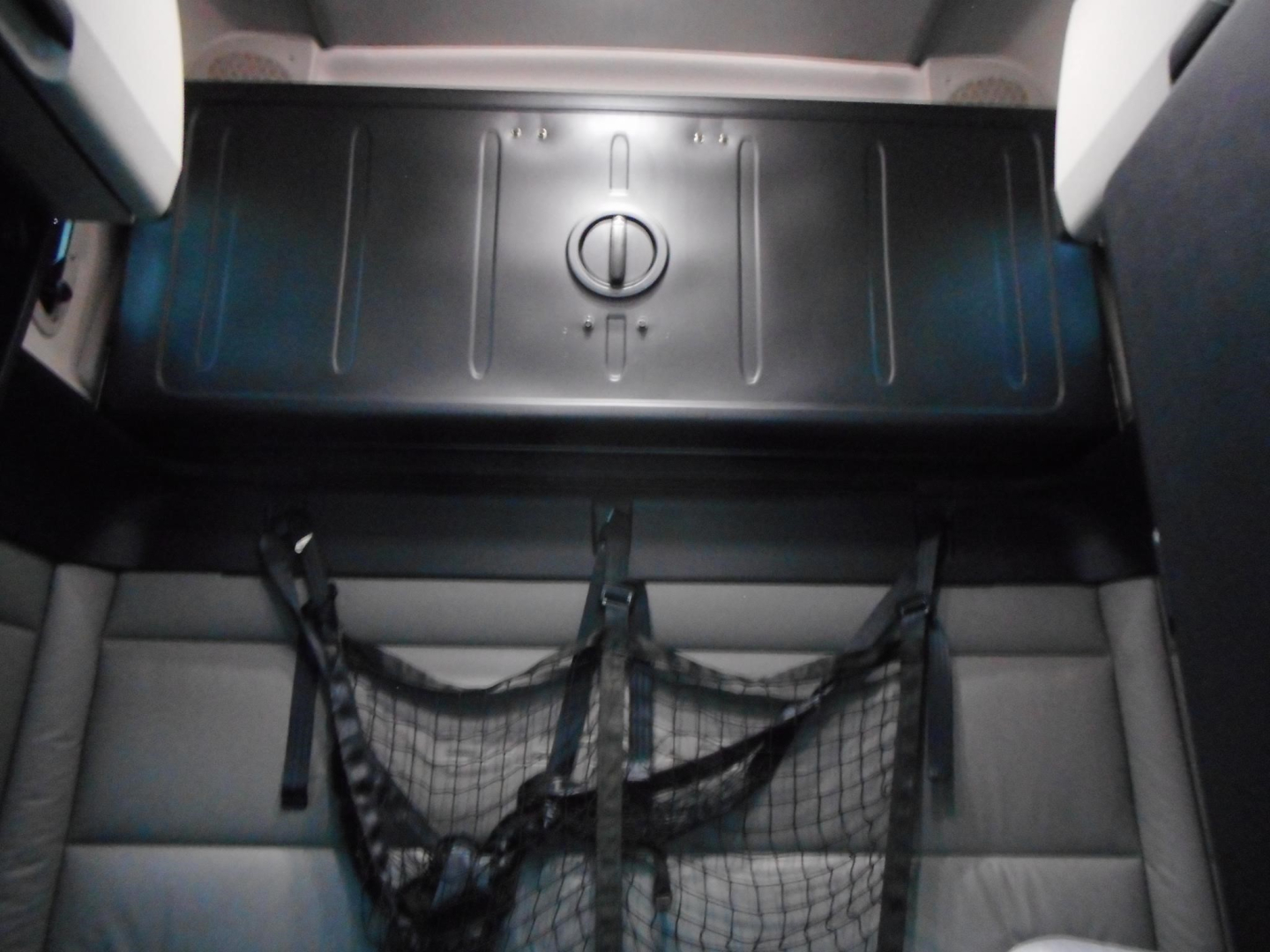 Cargo area of a 2022 Freightliner Cascadia 126 sleeper showing a black plastic storage bin with a circular latch and a cargo net on the seat base.