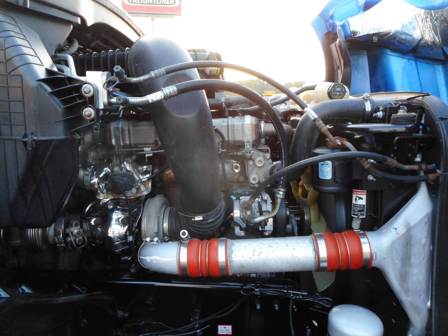 Engine bay of a Freightliner Cascadia 126 showing intake piping, hoses, and engine components with a red-and-silver exhaust pipe wrap.