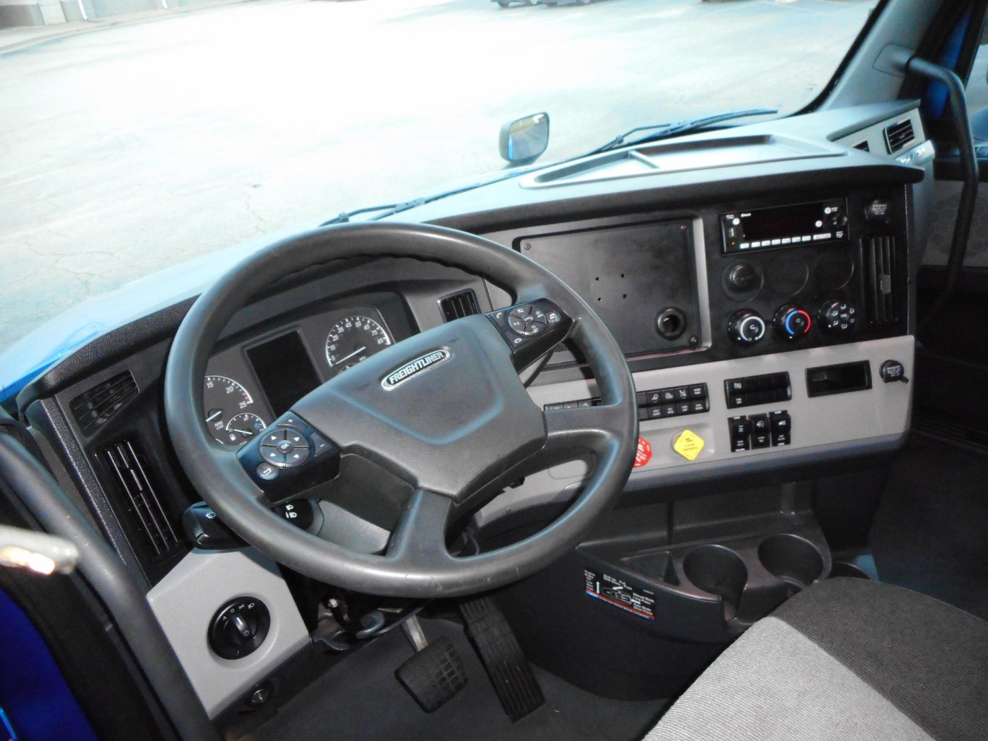 Cab interior of a Freightliner Cascadia truck showing steering wheel, dashboard, and center console with gauges and controls.