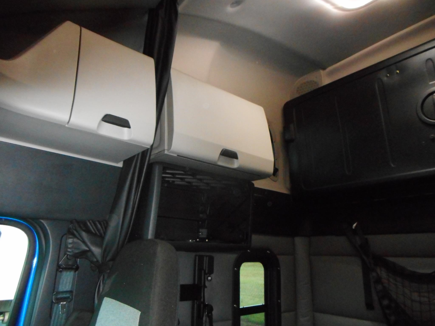 Cab interior of a Freightliner Cascadia showing overhead storage compartments and sleeper area with a window visible