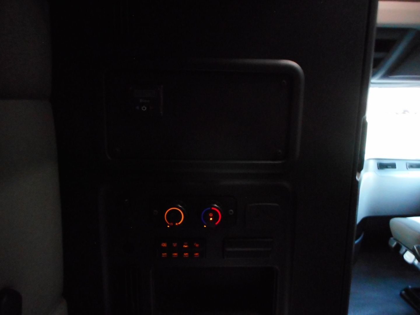 Cabin area of Freightliner Cascadia interior with climate control knobs and a small panel, dimly lit.