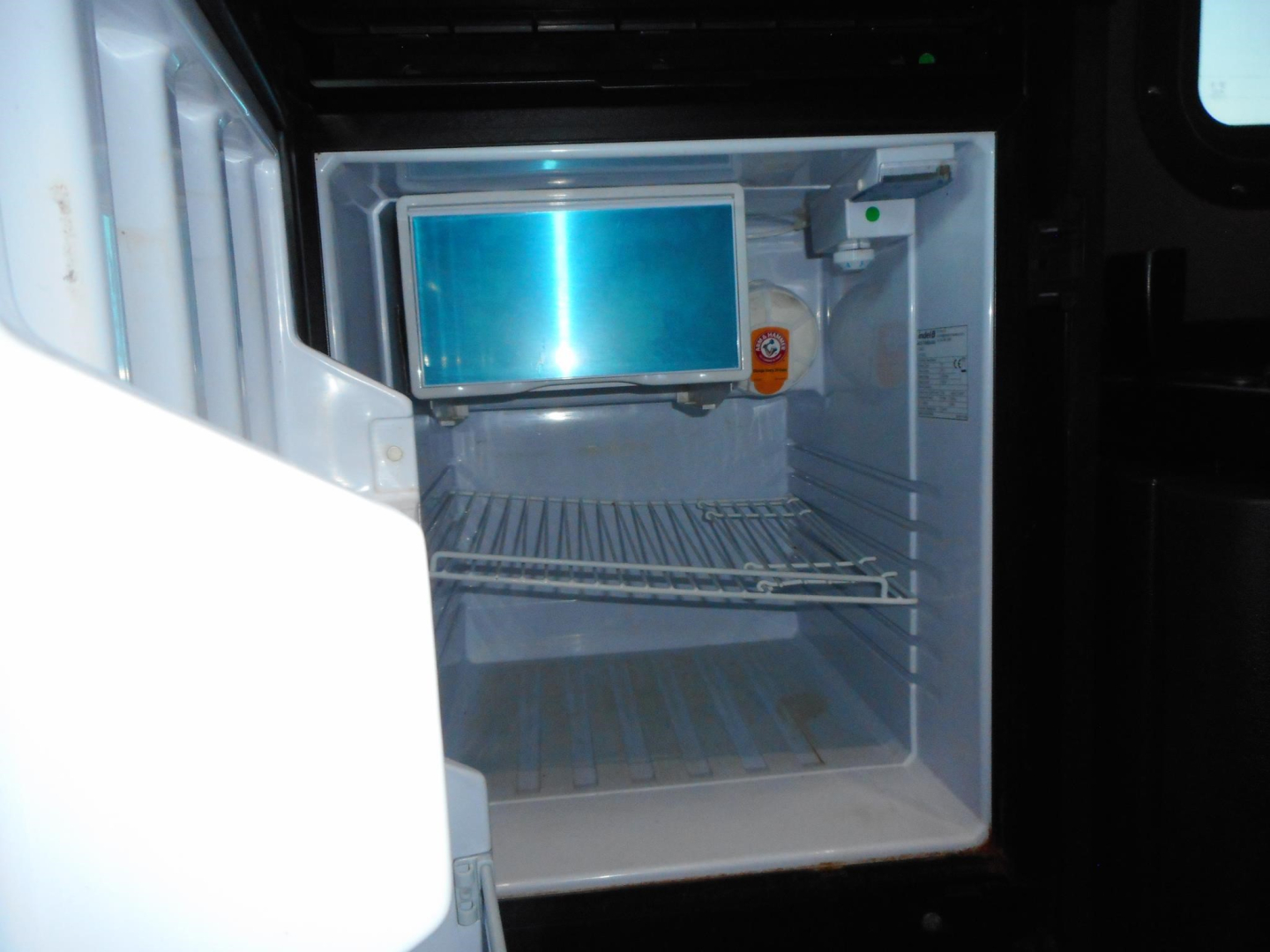 Fridge inside a Freightliner Cascadia sleeper cab showing a small built-in refrigerator with a freezer compartment and a blue-lit interior. Open door visible.