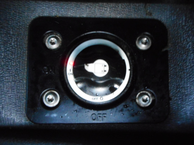 Circular switch with OFF/ON markings mounted on a textured surface, four screws at corners, small water droplets around, close-up view.