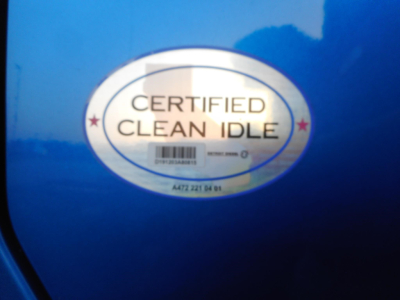 Certified Clean Idle oval badge on blue vehicle surface with barcode and text