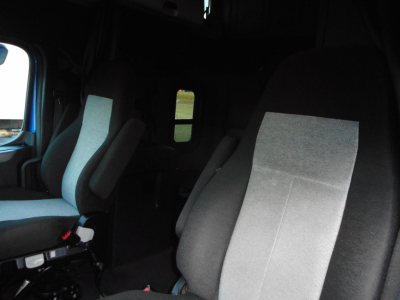 Truck cabin interior of a 2022 Freightliner Cascadia 126, front seats visible with light gray fabric, optional window in background.
