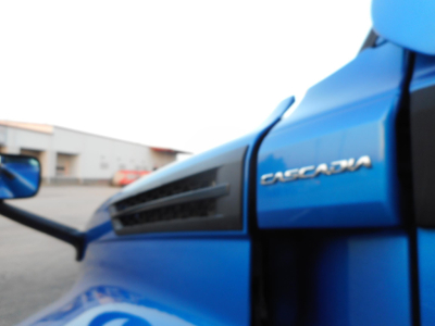 Freightliner Cascadia 126 badge on blue truck cab showing side view mirror and vent detail.