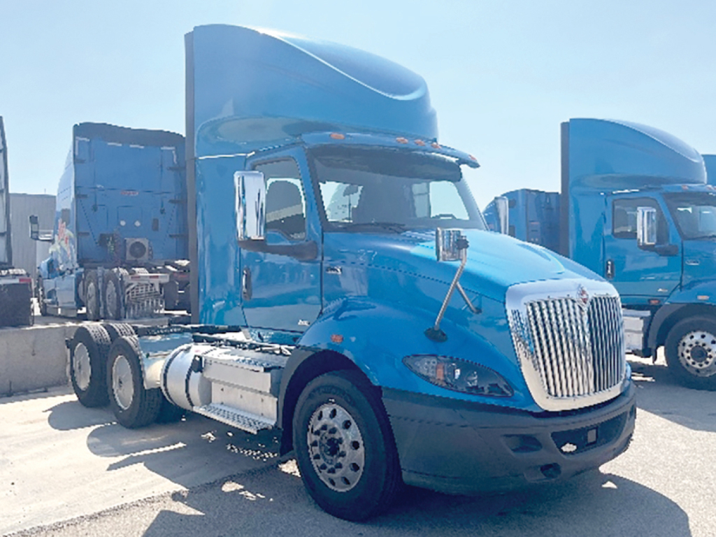 Truck cab and chassis of a blue 2019 International RH613 conventional daycab from a side angle showing fuel tanks and grille, in-service condition.
