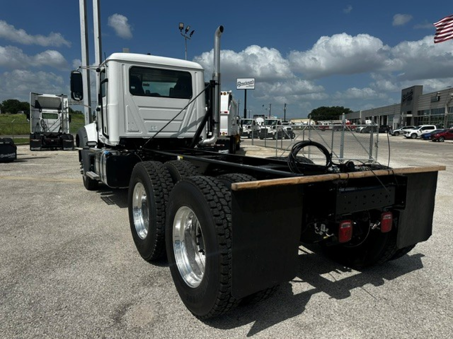 Dump truck chassis showing rear view with dual rear axles and flatbed mounting, white cab, black chassis guards and rear tires.