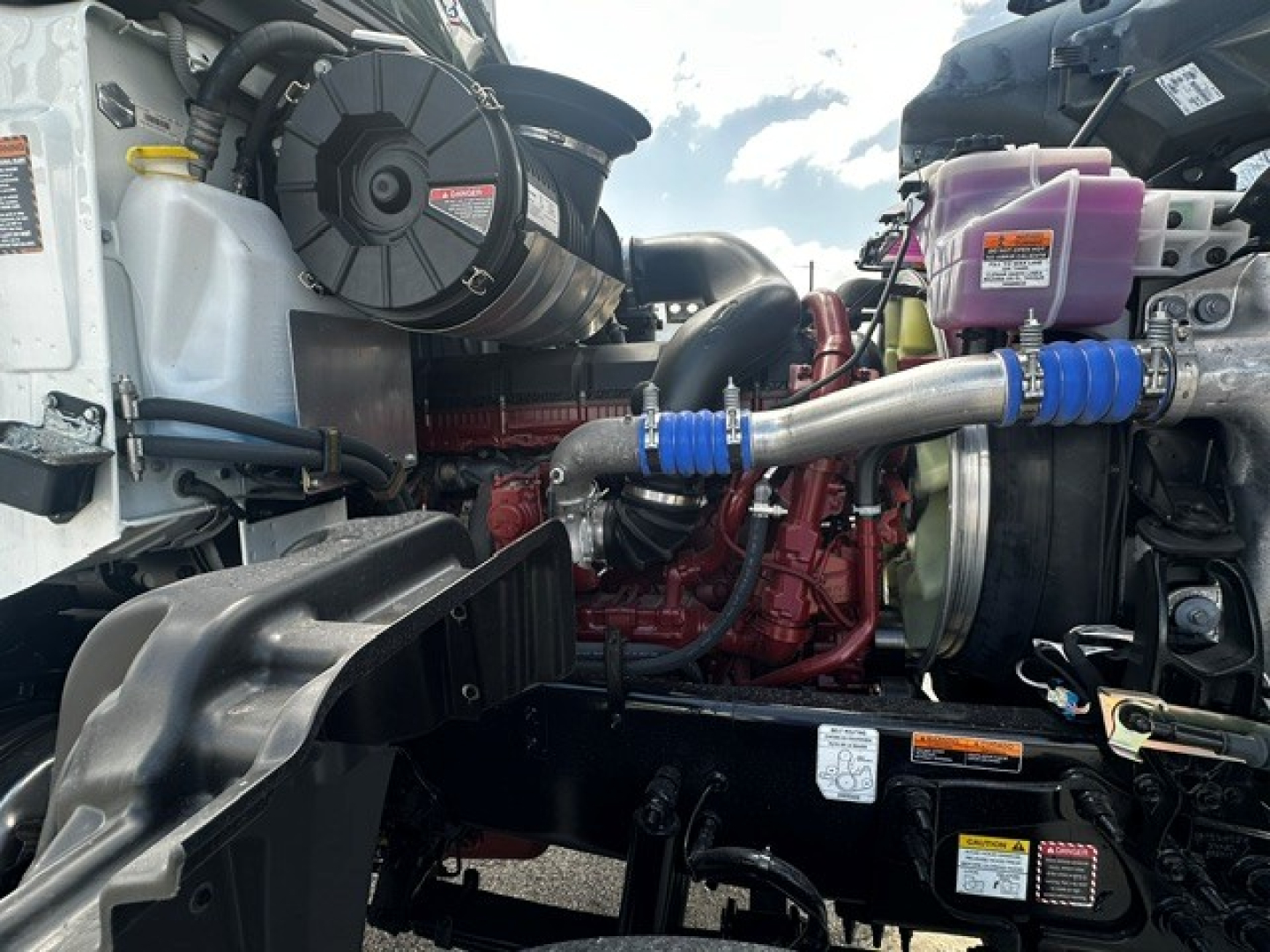 Mack GR64F engine bay showing coolant reservoir, turbocharger, hoses, and VCM components in a truck engine compartment.