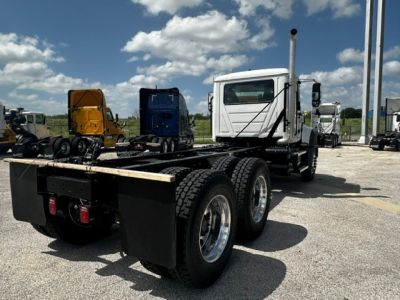 Tractor unit rear view showing chassis and double rear axles with black frames and white cab in a truck yard.
