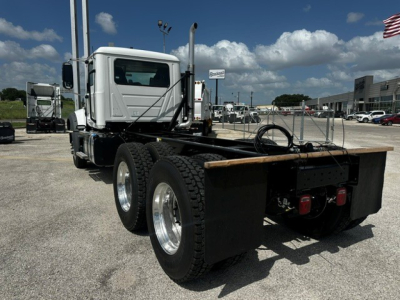 Dump truck chassis showing rear view with dual rear axles and flatbed mounting, white cab, black chassis guards and rear tires.