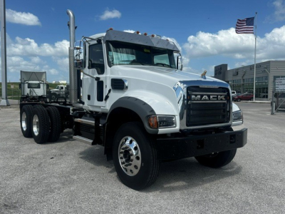 Mack GR64F truck cab front-right view showing chrome grille, large tires, and side exhaust; white cab with black bumper and Mack emblem.