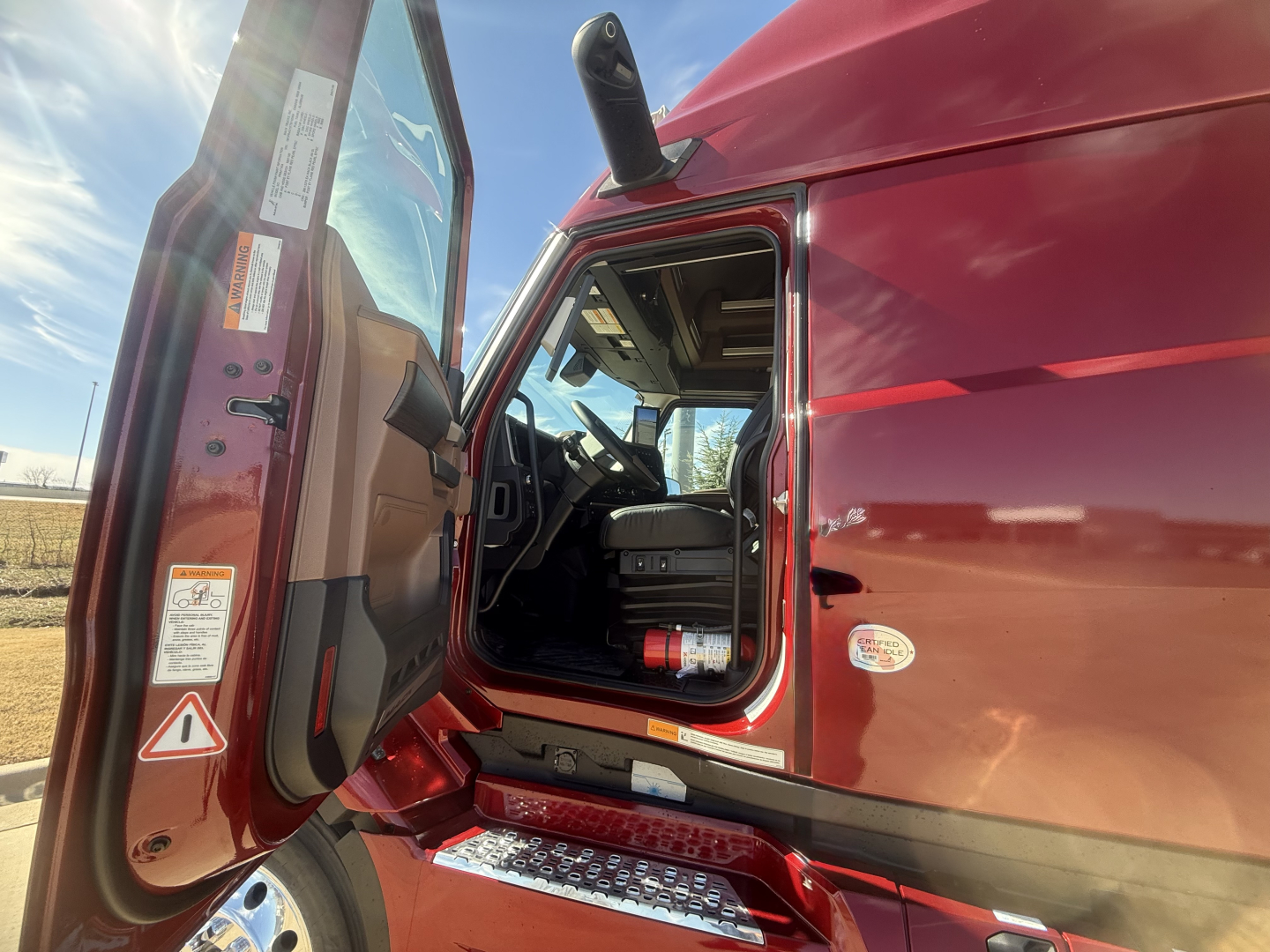 Truck cab interior with open door showing Mack PR64T76H exterior, red paint, step, and dashboard visible.
