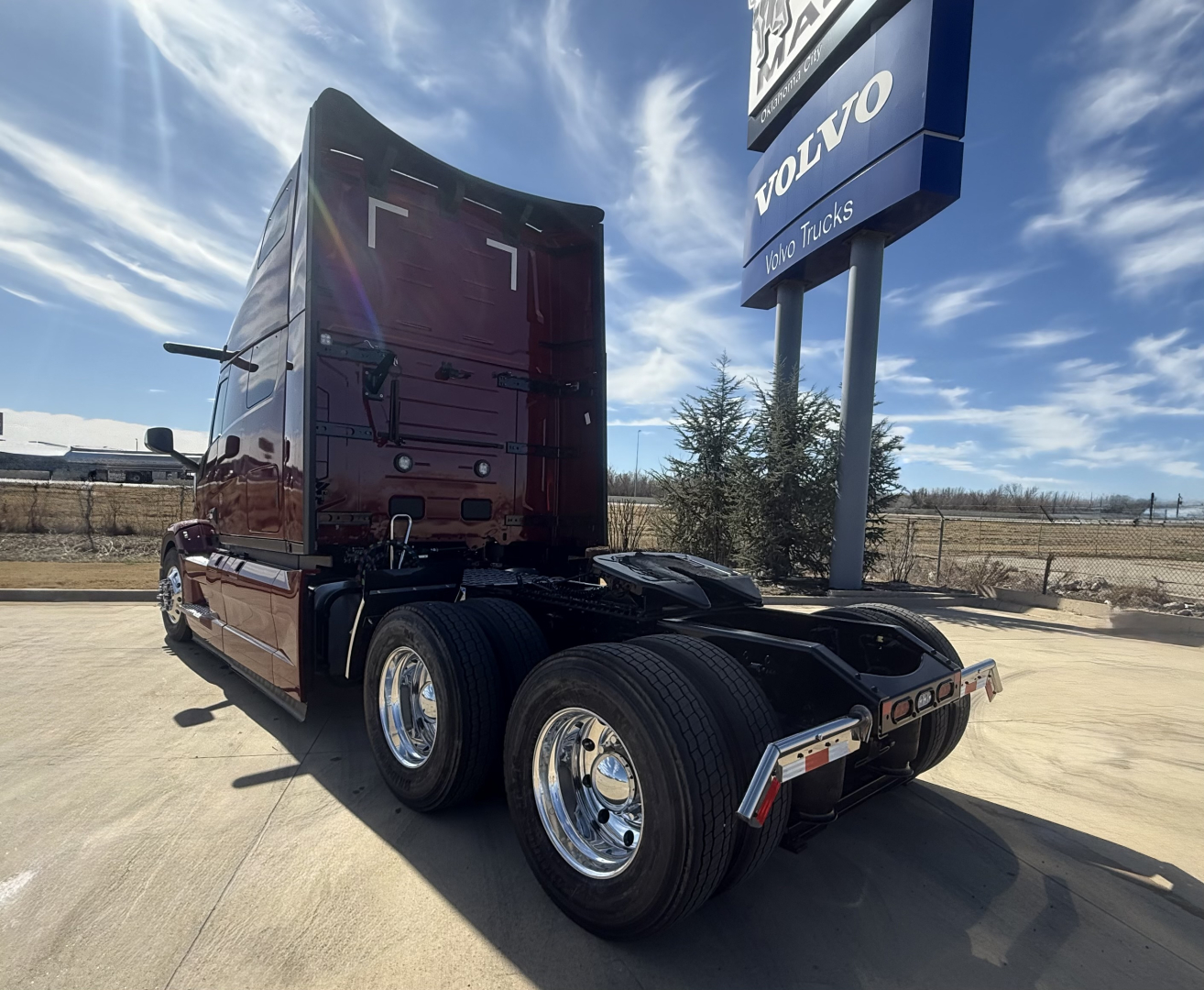 Mack PR64T76H conventional sleeper tractor rear view showing dual rear axles and chrome wheels under a sky with Volvo Trucks sign.