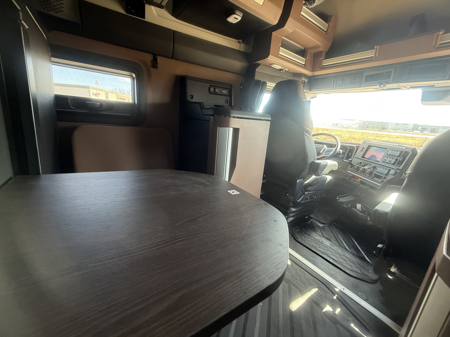 Interior cab of a 2026 Mack PR64T76H truck showing a dark wood table, overhead storage, and driver area with dashboard and steering wheel.