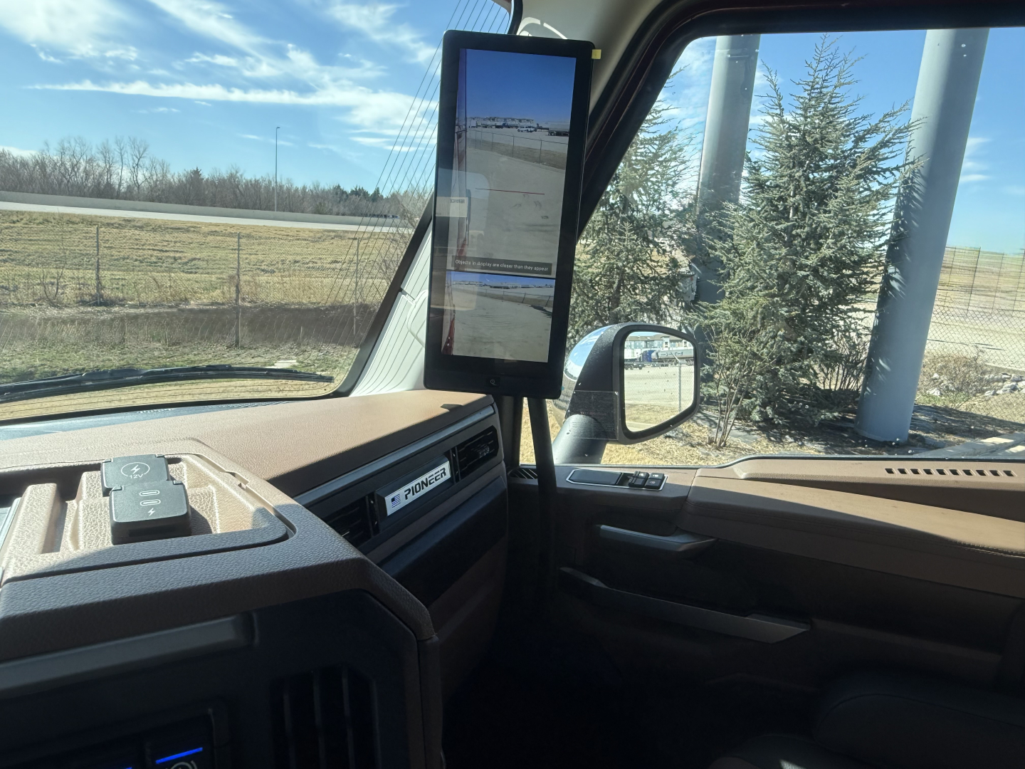 Interior view of a Mack truck cab showing a mounted tablet display on the A-pillar, dashboard with vents and control panel, side window, and mirror.