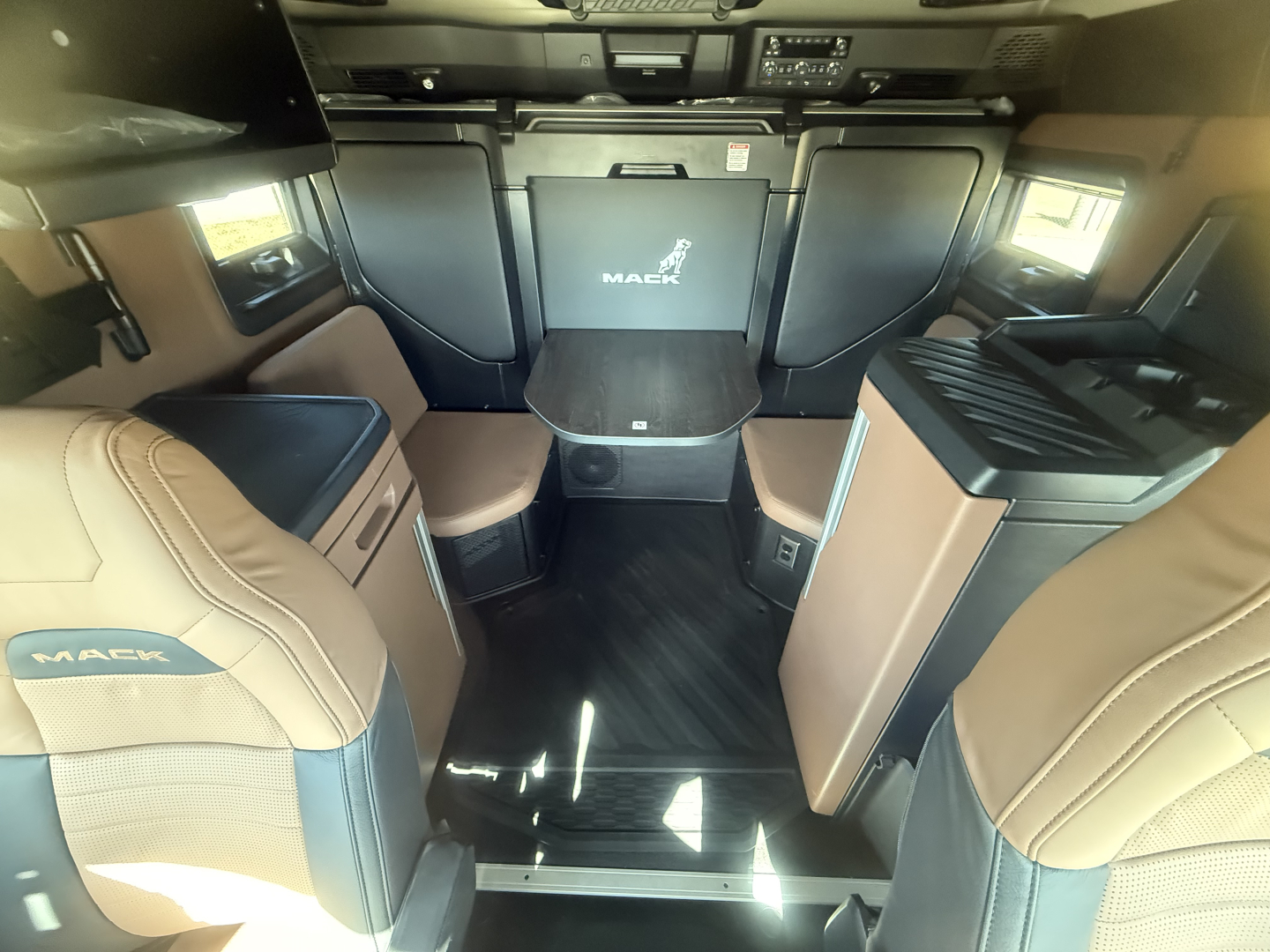 Mack PR64T76H conventional sleeper truck interior showing cockpit area with center table, captain seats, and side cabinets.
