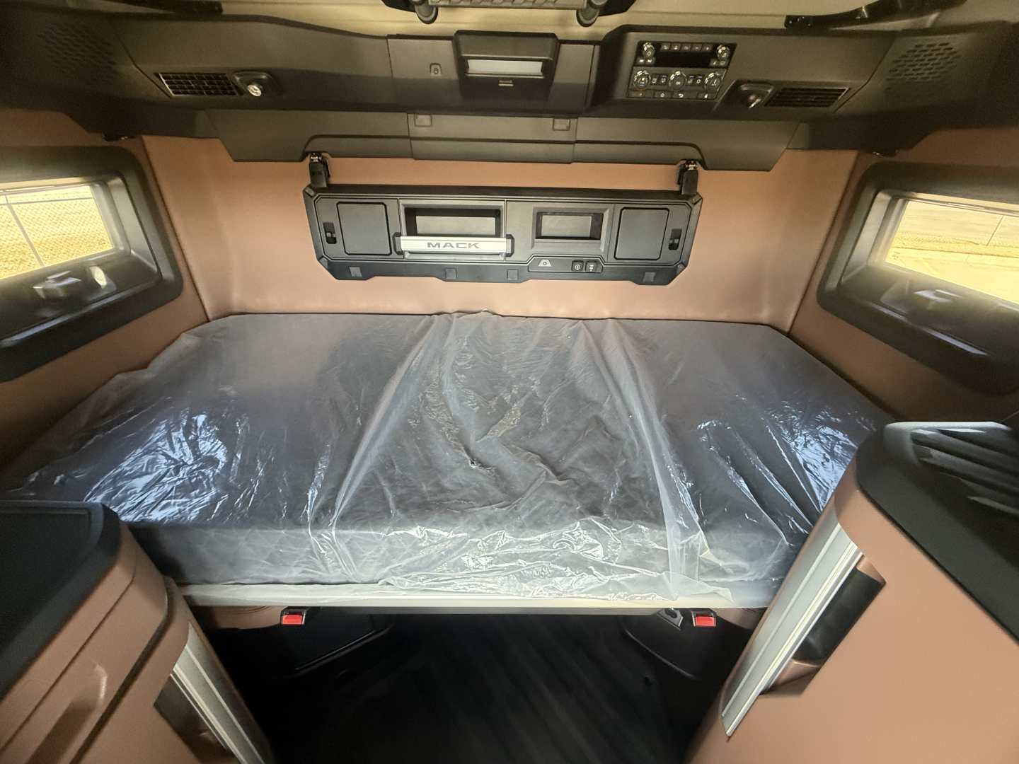 Mack PR64T76H truck cab sleeper interior with bed, dashboard controls, and protective covering over the mattress.