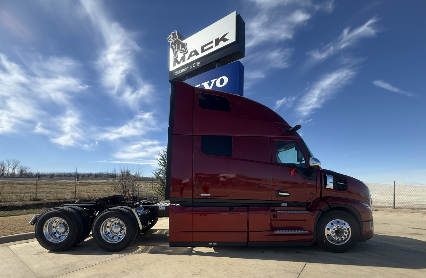 Mack PR64T76H truck tractor side view showing red cab and sleeper with chrome wheels at a dealership