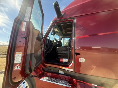 Truck cab interior with open door showing Mack PR64T76H exterior, red paint, step, and dashboard visible.