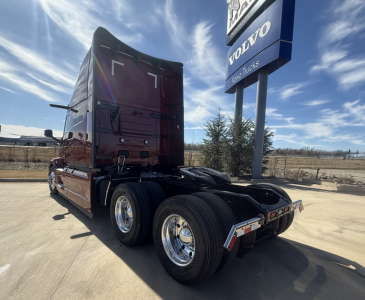 Mack PR64T76H conventional sleeper tractor rear view showing dual rear axles and chrome wheels under a sky with Volvo Trucks sign.