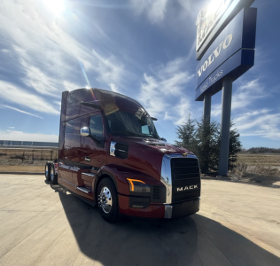 Mack PR64T76H truck in a dealership lot showing front grille with MACK badge and maroon cab.