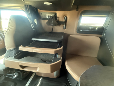 Cab interior of a 2026 Mack PR64T76H showing fold-out storage drawers, a mounted monitor, and a seating area with tan upholstery in a sleeper cab.