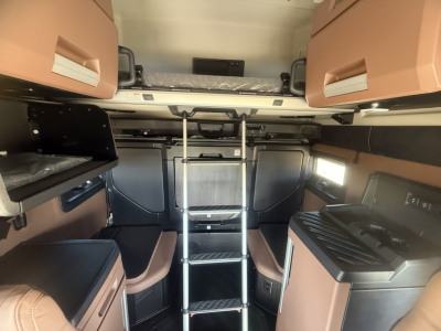 Truck cab interior of a 2026 Mack PR64T76H sleeper showing bunk area, ladder, overhead storage, and side cabinets with tan upholstery.