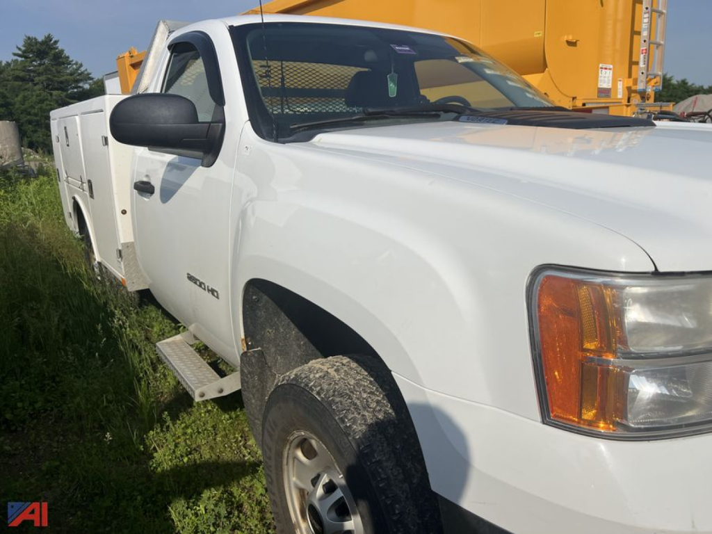 GMC Sierra 2500HD utility truck in white with extended cab, side steps, utility chest on bed, front right angle view.